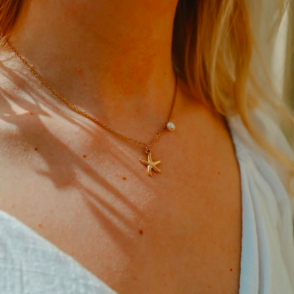 Gold starfish pendant necklace with a freshwater pearl worn at the neck