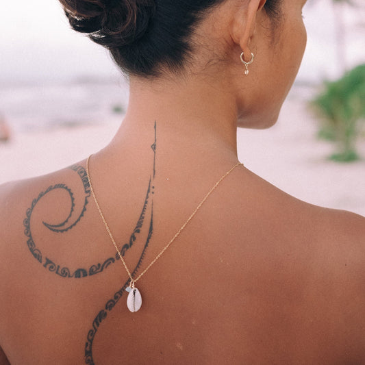 Cowrie shell and raw birthstone necklace on a gold chain worn at the neck