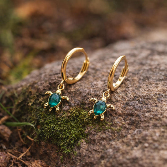 Gold sea turtle charm huggie hoop earring with a green gemstone worn on the ear