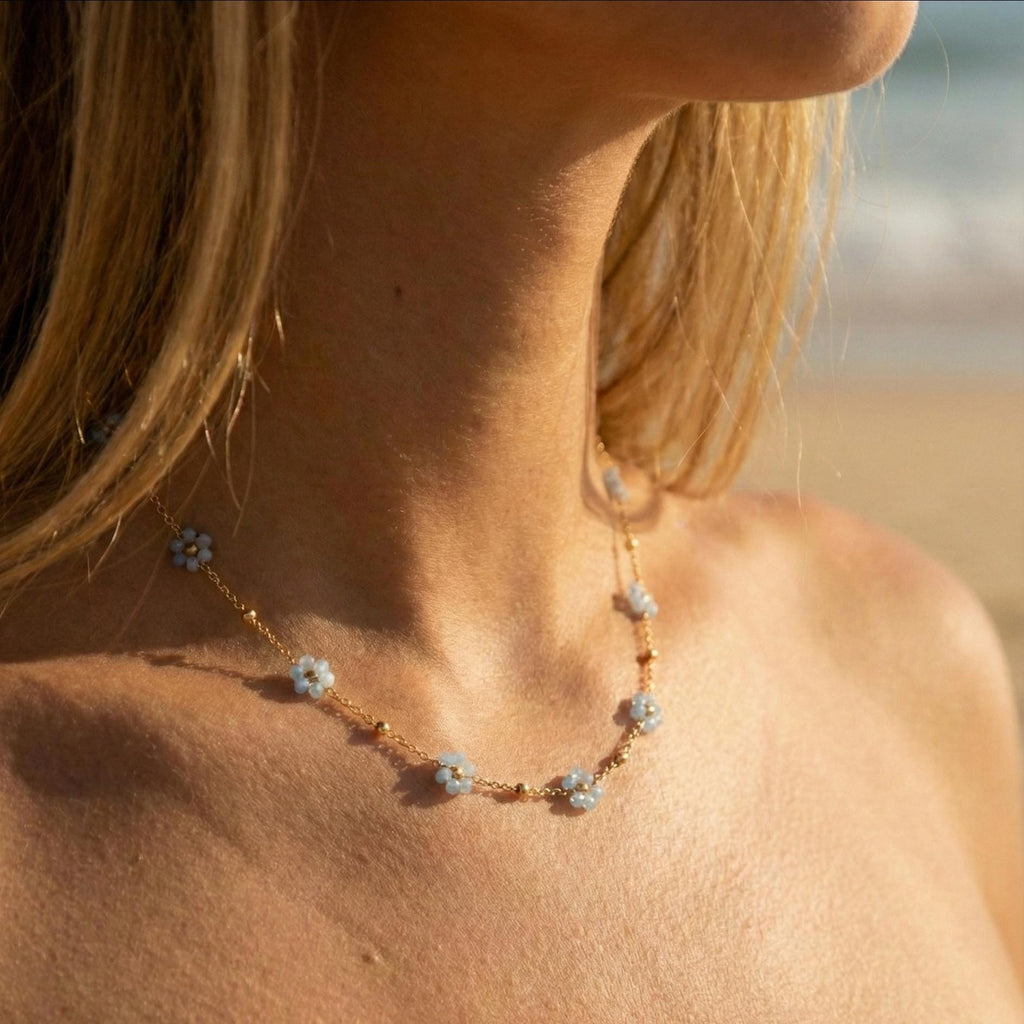 Gold daisy flower pendant necklace with an aquamarine bead worn at the neck