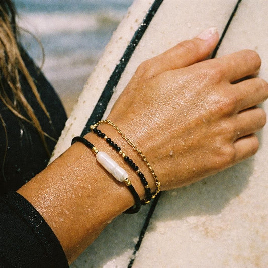 Black onyx and pearl beaded bracelet on a gold chain worn on a wrist