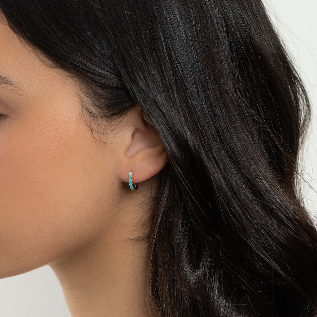 Gold huggie hoop earring set with blue opals worn on the ear